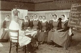 (Schwarz-Weiss-Foto vpn 1926) Arzt im Kittel unterichtet eine Gruppe von Diakonissen. Rechts im Bild steh eine Tafel, links eine Abbildung von der Lunge sowie ein Skelett