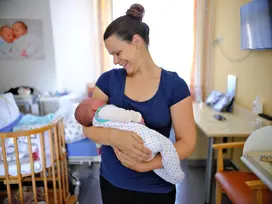 Glückliche Mitter im blauen T-Shirt hält ein neugeborendes Baby auf dem Arm und strahlt es an