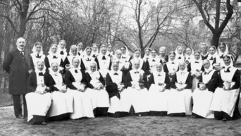 Gruppenfoto 32 Diakonissen in Trachten und ein Herr im Anzug im Garten (Schwarz-Weiss-Foto)