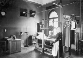 Man sieht eine Diakonisse, die eine Untersuchung an einem Patienten durchführt. die Hand scheint verletzt zu sein. Vermutlich eine Röntgen aufnahme der Hand. (Schwarz-Weiss-Foto)