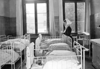 Neugeborenden Station. Viele kleine Bettchen in einem Raum, eine Diakonisse versorgt die Babys (Schwarz-Weiss-Foto)